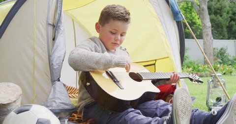 Caucasian boy sitting in tent in garden and playing guitar. spending time alone at home.