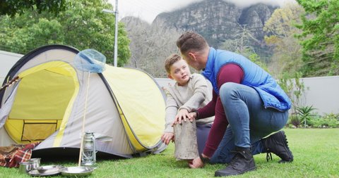 Happy caucasian father with son preparing camp with tent in garden. family spending time at home.