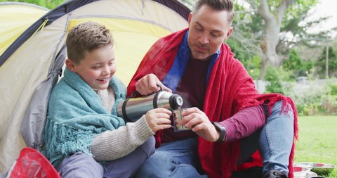Happy caucasian father with son sitting in tent and drinking tea in garden. family spending time at home.