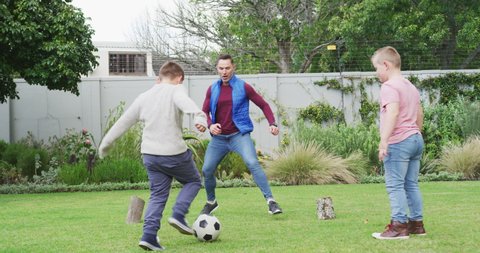 Happy caucasian father with two sons playing football in garden. family spending time at home.