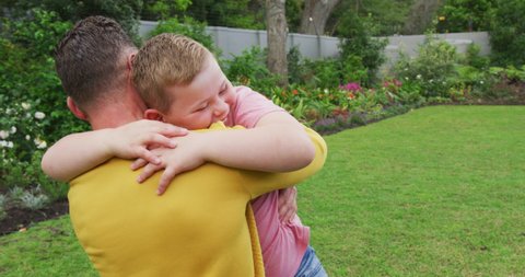 Happy caucasian father with son embracing and carrying in garden. family spending time at home.