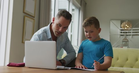 Caucasian father with son sitting at table and learning with laptop at home. family spending time at home.