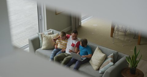 Caucasian father with two sons sitting in living room and using laptop. family spending time at home.
