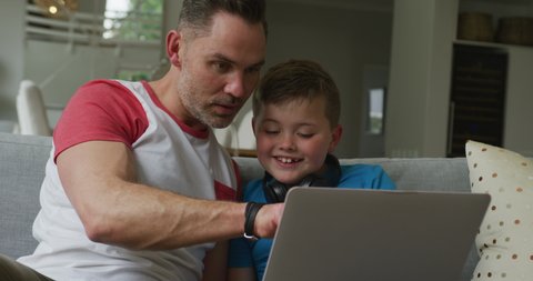 Caucasian father with son sitting in living room and using laptop. family spending time at home.