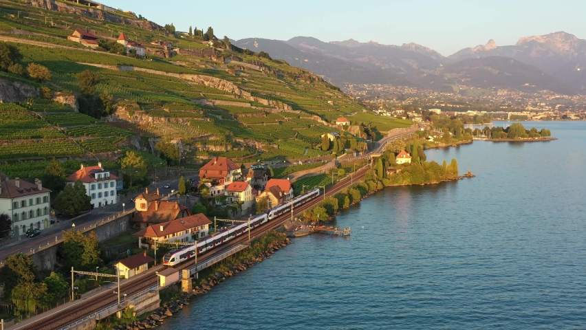 Aerial drone footage of a commuter train riding along the Lavaux famous terrace vineyard by lake Geneva between Montreux and Lausanne in Switzerland. 