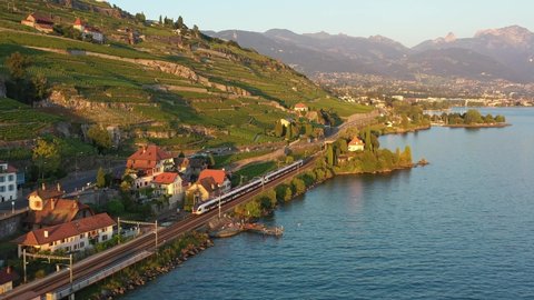 Aerial drone footage of a commuter train riding along the Lavaux famous terrace vineyard by lake Geneva between Montreux and Lausanne in Switzerland. 