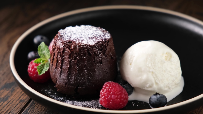 Chocolate fondant cake with scoop of vanilla ice cream. Pouring chocolate sauce on ice cream. Sweet dessert on plate