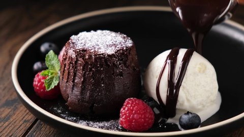 Chocolate fondant cake with scoop of vanilla ice cream. Pouring chocolate sauce on ice cream. Sweet dessert on plate