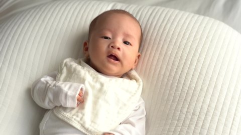 Newborn Asian baby sneezing while lying on a white cushion 