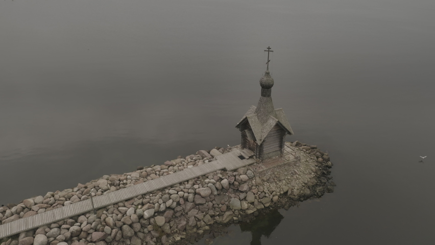 Small Russian wooden church on the seashore. Dark inclement weather, gray sky. Taken from a drone.