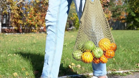 Woman walks with a braided string bag of fresh fruit. Life without plastic waste. Low-waste lifestyle. Sustainable ecological lifestyle
