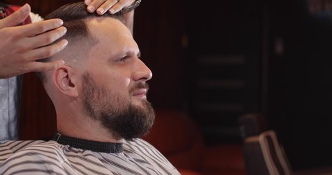 Close-up of a handsome Caucasian guy sitting in a hairdressing salon. An unrecognizable barber making styling. 4K 50 fps slow motion