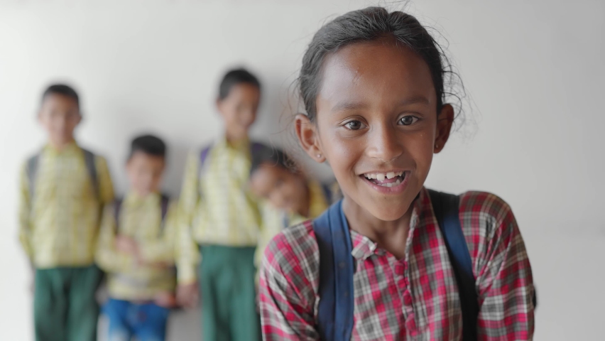 Close shot of a young little adorable primary school girl wearing a school uniform with backpack smiling joyfully staring at the camera standing in classroom learning and education concept Royalty-Free Stock Footage #1080285344