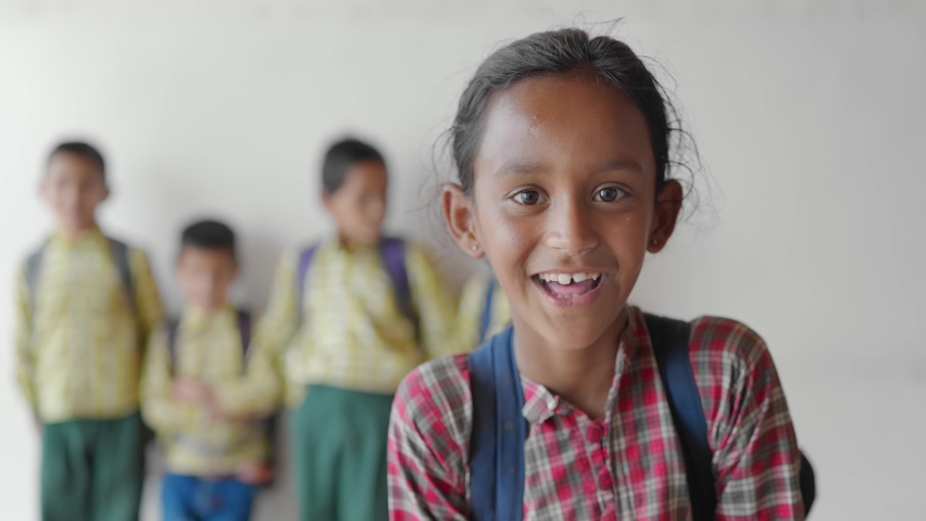 Close shot of a young little adorable primary school girl wearing a school uniform with backpack smiling joyfully staring at the camera standing in classroom learning and education concept | Shutterstock HD Video #1080285344