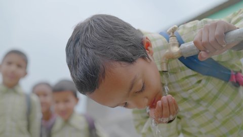 close up shot of a young little school boy with a backpack drinking clean water from a running tap in a rural village and his waiting for their in the back. Concept of a natural resources conservation: film stockowy