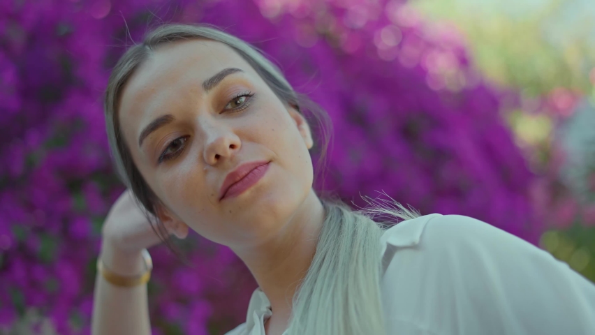 Beautiful young woman with blond hair taking photo with flowers. She is smiling and happily posing. Portrait of happy young woman. Slow motion video.