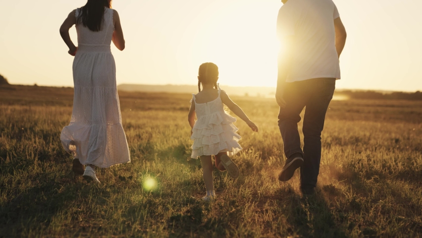 a little laughing girl runs with her parents at sunset, a happy family, a childhood dream, kid running in sunshine with mom and dad, playing catch-up with child, father and mother with baby daughter Royalty-Free Stock Footage #1080288146