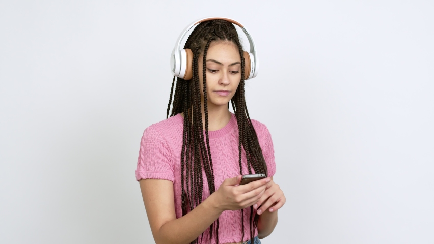 Teenager girl with braids listening music with a mobile and dancing over isolated background