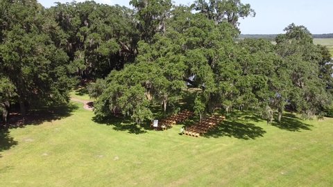 Top view of the wedding venue in a green field under the tree. Tradition of wedding ceremony with decorated decor on the lawn. Rows of festive chairs and beautiful flowers in baskets. Lake shore