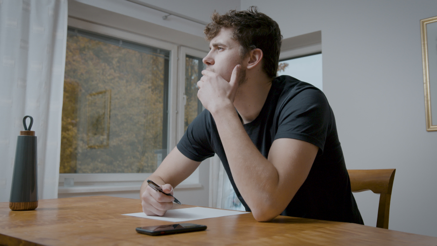 Caucasian Male Sitting Behing The Desk And Thinking About Ideas And Thoughts To Write On A Paper Or Document.