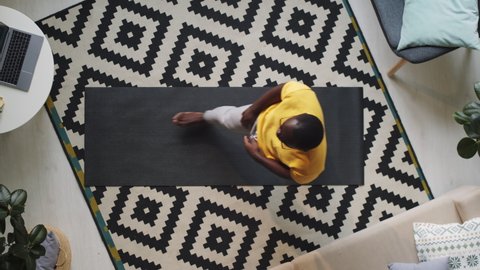 Overhead shot of barefoot African American man in sportswear exercising on mat in living room at home