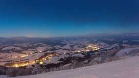 Time Lapse Video with Blue Sky, Fog and Snow of a starry sky over snowy ski resort in the mountains. Scenic Aerial View of High Mountains Peaks Range. Carpathian Mountain in Ukraine.