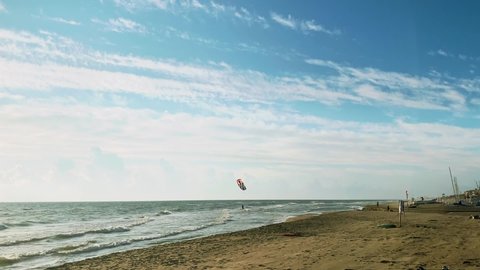 Kitesurfer on the crest of a wave. Blue sky with white clouds. Seascape with kitesurfers in the waves. Colorful kitesurfing sail fly in the cloudy sky. 