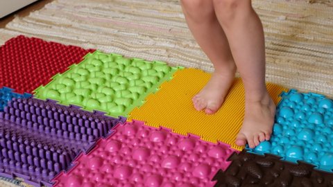 The child jumps on the puzzle details of an orthopedic massage mat with a soft, pleasant surface in the form of grass. tactile play mats