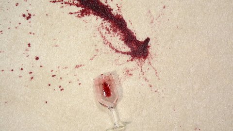 A glass of wine spilled on white carpet shown in slow motion