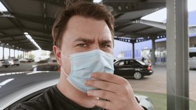 Young man removes protective medical mask from his face so that it is more convenient to talk. Male blogger shares interesting and useful information in his vlog, gesturing in the parking lot.
