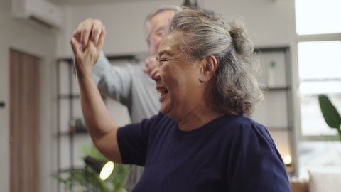 Slow motion Asian mature senior couple is dancing and smiling at home.