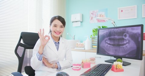 asian female dentist works at dental clinic showing teeth xray - she looks at camera smily with crossed arms