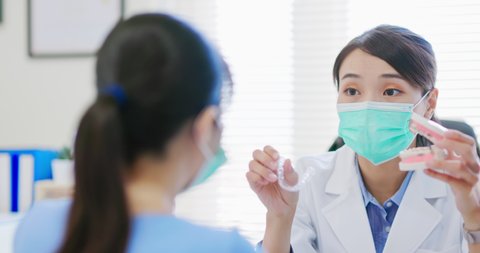 close up of asian female dentist explains patient for orthodontic treatment by denture model and invisible braces while they wear protective face mask to prevent COVID19