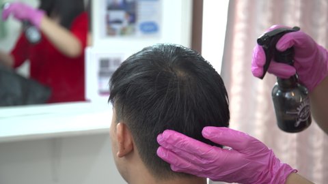 Footage showing a modern hair stylist spraying a water on the handsome Asian man customer head before doing a hair dressing. Man having a hair cut service in beauty hair and salon.