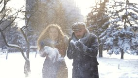 Slow motion. A beautiful young guy and a girl throws snow into the air. A romantic couple is having a good time in a snowy city park in the cold winter. A tender relationship between lovers.