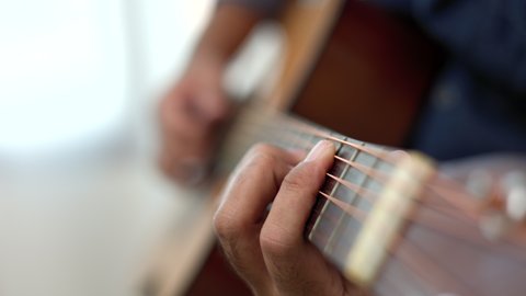Lifestyle concept. Young asian musician playing guitar in living room at home on this weekend. Relaxing with song and music. Asian man having fun playing acoustic guitar
