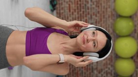 Female in sportswear Listening to Music on modern Headphones. Fitness woman taking break during workout. Overjoyed young woman listening music in headphones and resting after workout. vertical video