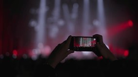 concert, hands with a mobile phone filming video of a scene with multicolored spotlights at night