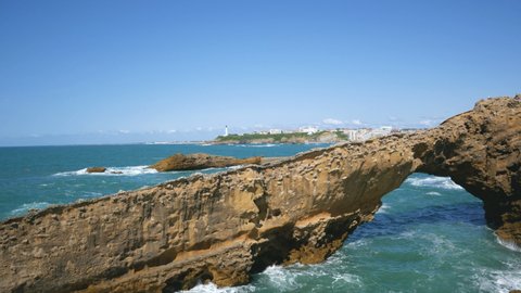 The coastline of the famous Biarritz in summer (Aquitaine, France), with atlantic ocean waves crushing on the beautiful cliffs. A lighthouse is visible in the distance. Blue sky on the background.