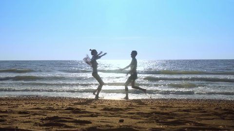 young sexy couple, woman and man, run towards each other, jump on waves on seashore. against background of blue sea horizon with sky. They fool around and have fun on beach. sunset.