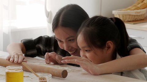 Korean Mom And Little Daughter Baking Cookies Rolling Up Dough And Smiling In Modern Kitchen At Home. Asian Mom And Her Child Making Pastry Together. Family Weekend, Nutrition Concept