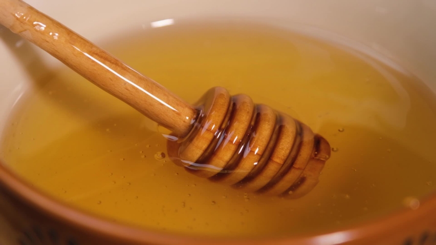 Liquid Organic Honey on a Wooden Spoon in a Bowl Close Up Shot. Healthy Food Concept. Slow motion of dripping honey. Fresh honey is poured on a wooden spoon. Natural production, honey advertisement. 