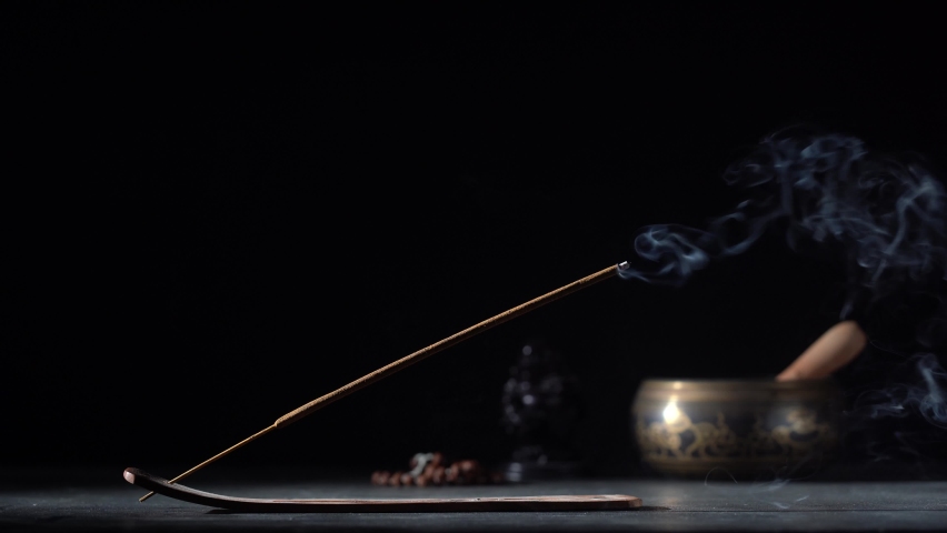 Asian incense stick in stick holder burning with smoke on black background, close up, copy space. Meditation, yoga, self development and sound therapy concept | Shutterstock HD Video #1080315278
