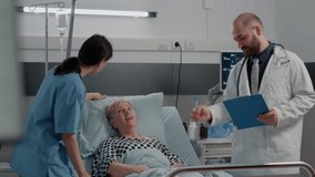 Medical team consulting aged woman with sickness in bed. Doctor talking to ill patient in hospital ward while nurse using oximeter for oxygen saturation measurement and healthcare. - Powered by Shutterstock - Get 15% off with code: PIKWIZARD15