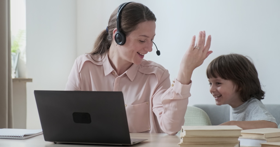 Young focused woman working remotely on laptop and chatting with colleagues. Little adorable son comes up playing naughty and mischievous. Perfect example of working together online and love in family Royalty-Free Stock Footage #1080325211
