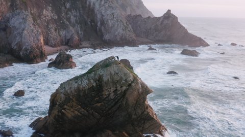 Aerial view of a fisherman at the top of a rock with endless ocean behind. Adult man catching fish on cliff with difficult access as seen from top. High quality 4k footage