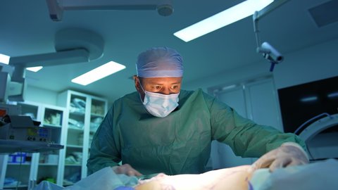 Portrait of a doctor doing liposuction procedure. Surgeon pumping fat from patient's abdomen on operating room background.