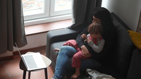 Mother and child sitting on sofa together watching media content on laptop computer at home