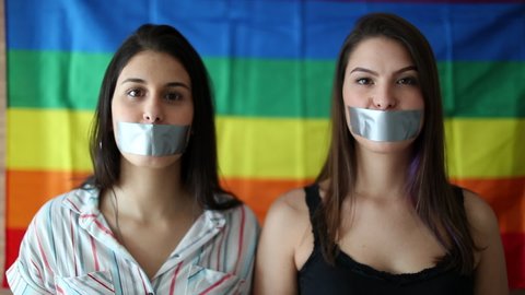 Two women looking at camera taping duct tape in mouth. LGBT censorship concept