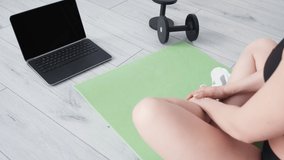 Online training. Sportive woman. Home gym. Healthy lifestyle. Unrecognizable lady sitting lotus pose sitting yoga mat looking laptop blank screen in light room interior copy space.